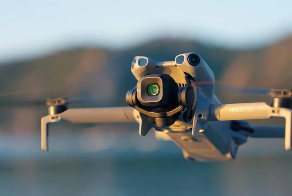 Nacelle et objectif d’un DJI Mini 5 Pro en vol, décor de montagne flou derrière