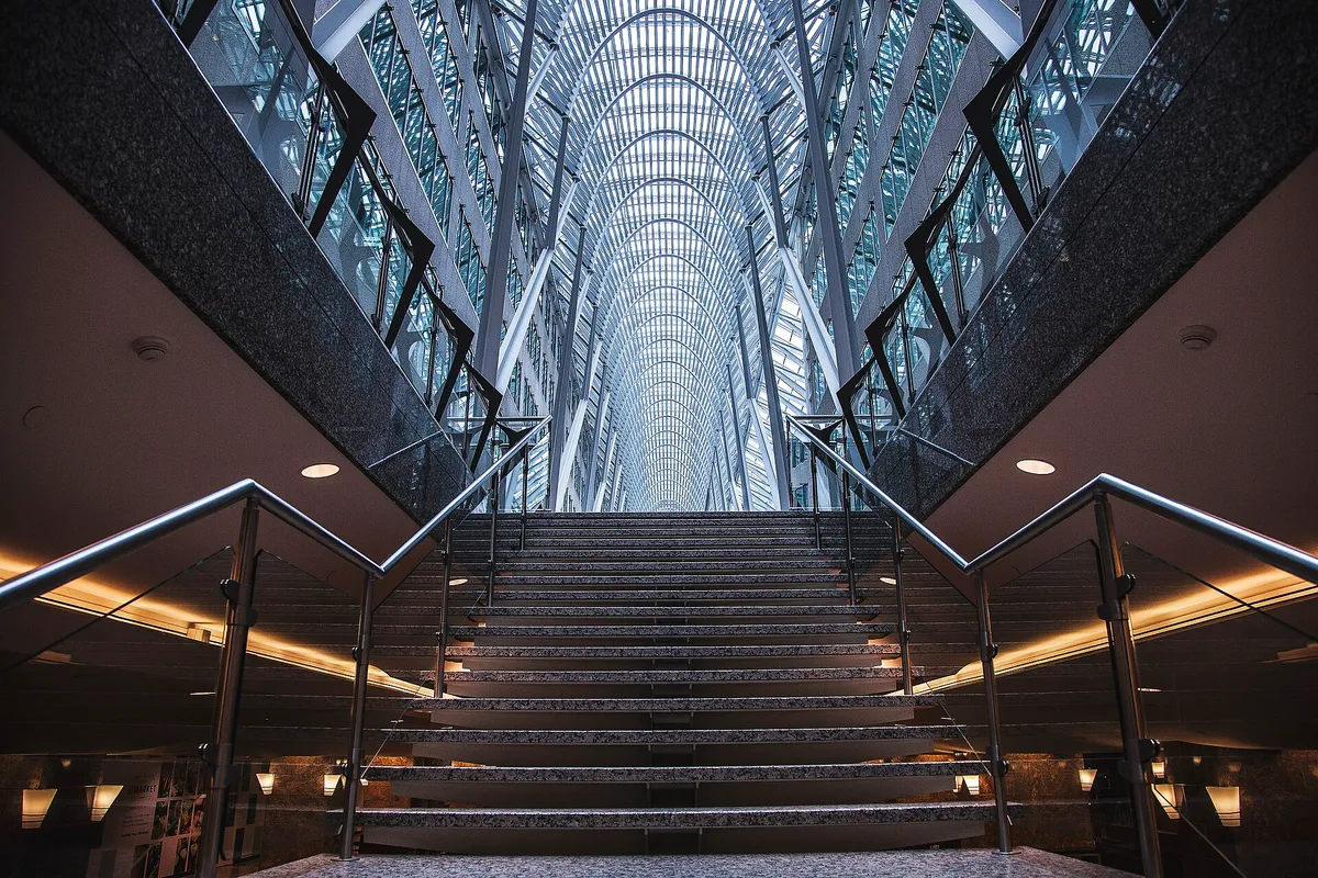 Hall d’immeuble tertiaire : un large escalier de pierre monte vers une galerie vitrée en voûte
