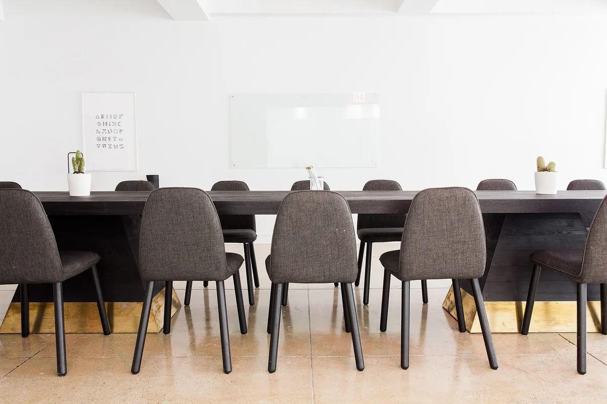 Salle de réunion vide : longue table, chaises grises, tableau blanc au mur