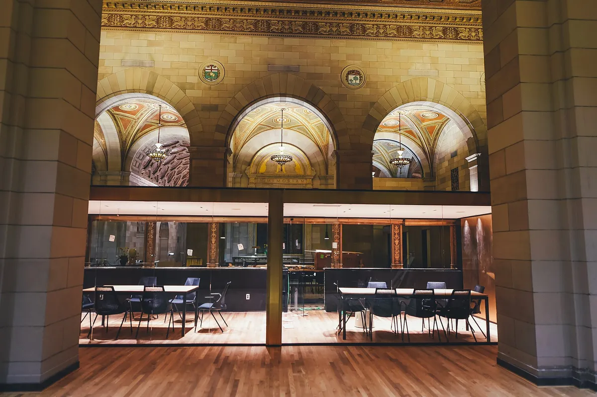 Hall à arcades vitrées, tables et chaises alignées derrière la verrière