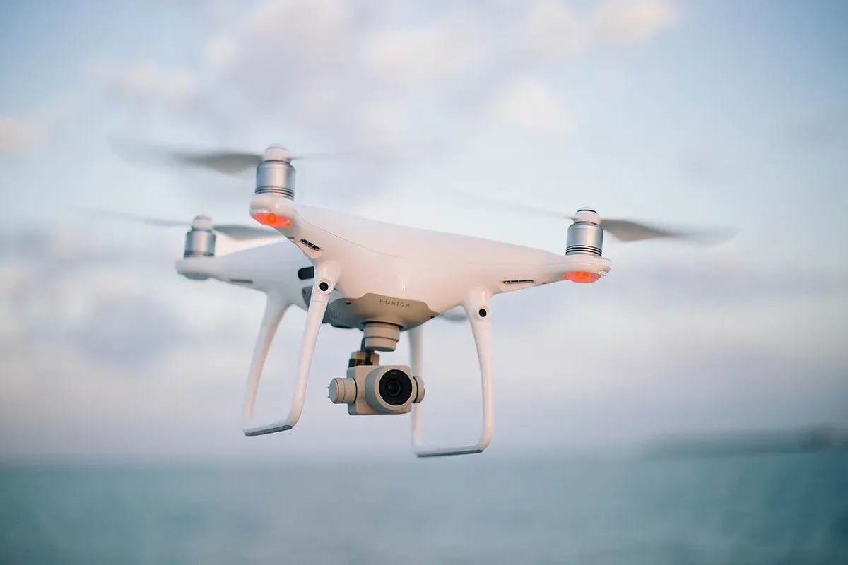 Petit drone blanc en vol dans un ciel bleu clair, caméra orientée vers le sol