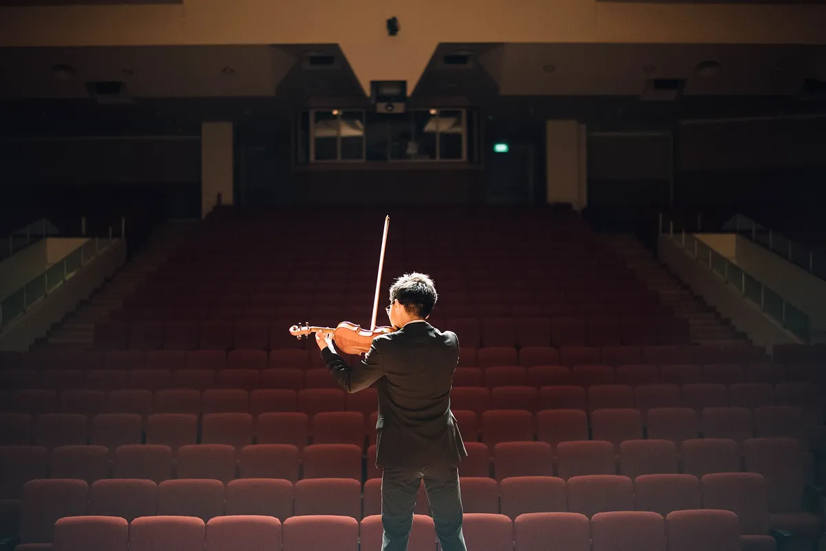 Violoniste seul sur scène face à une salle de fauteuils rouges vides