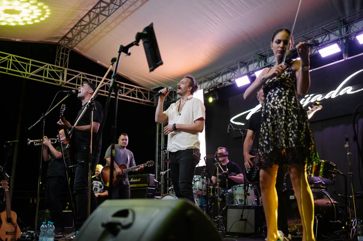 Grupo em concerto em palco coberto, cantor ao microfone em frente aos músicos