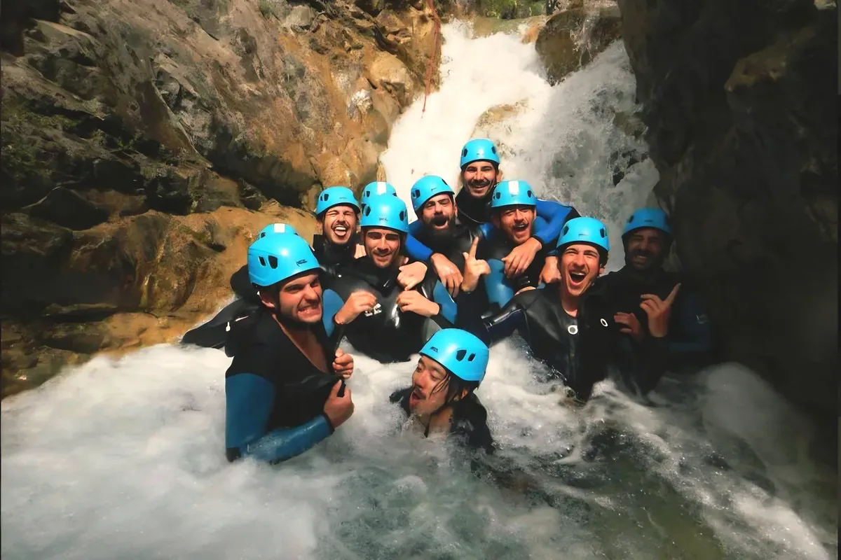 Groupe de canyonistes en combinaison et casque dans l’eau vive au pied d’une cascade