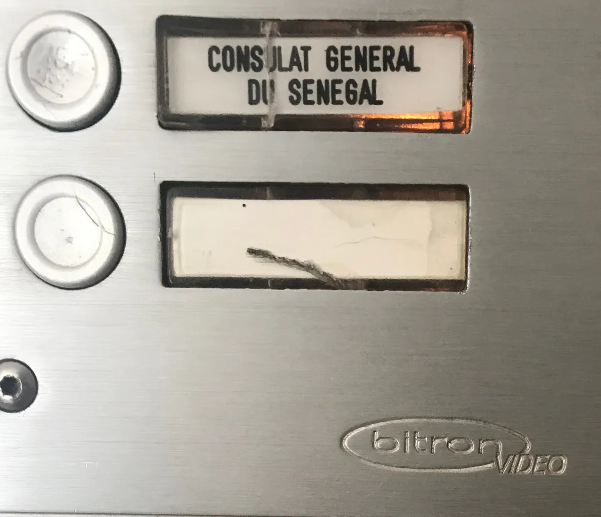 A stainless steel door entry panel with two round call buttons and their name holders