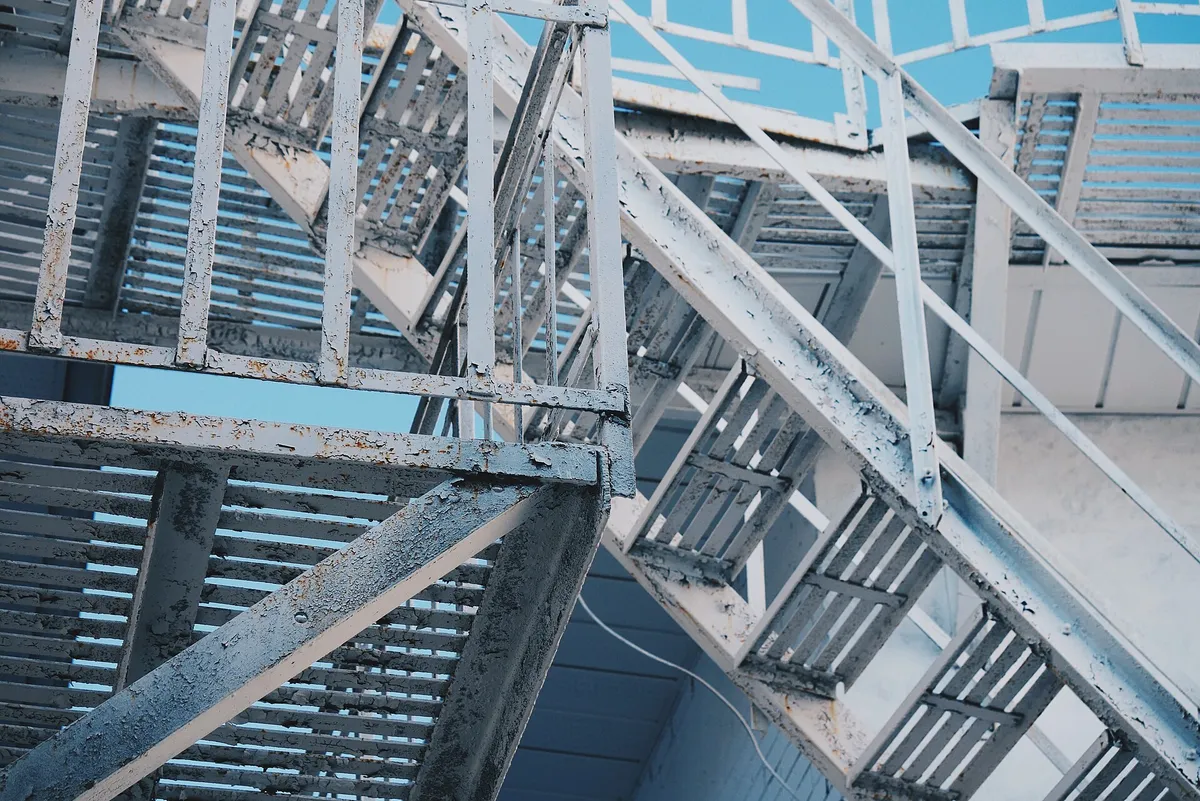 External metal staircases on a building, seen from below against a blue sky