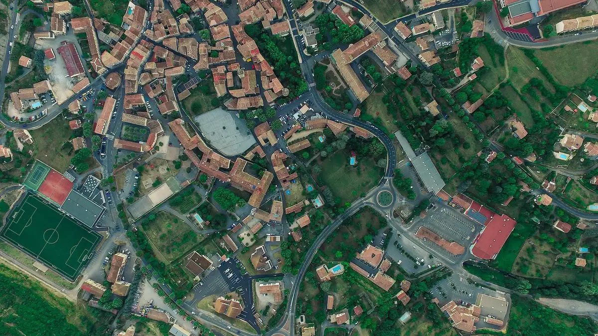 Vue quasi verticale d’un village du sud de la France : toits de tuiles, piscines et terrain de sport