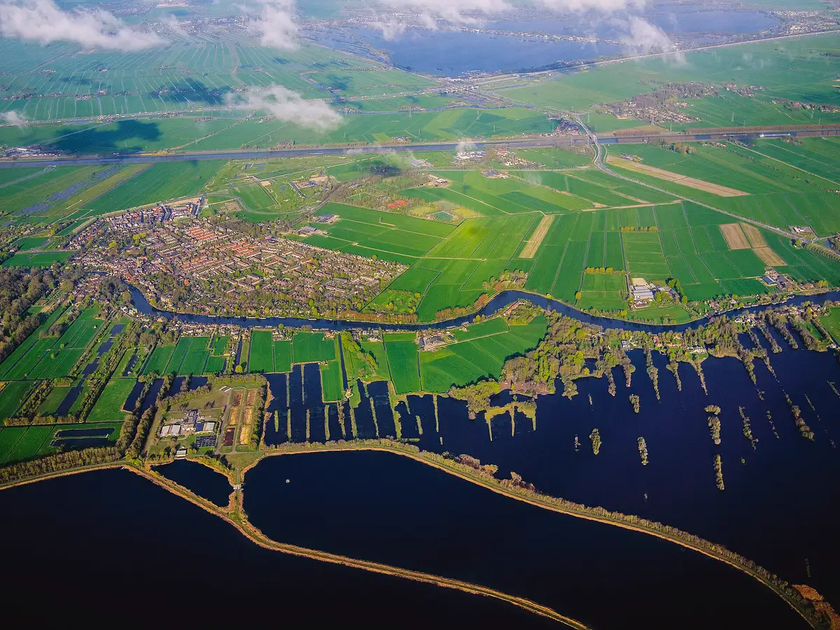 Village bordé d’un canal vu d’avion, entouré de champs découpés jusqu’à l’horizon