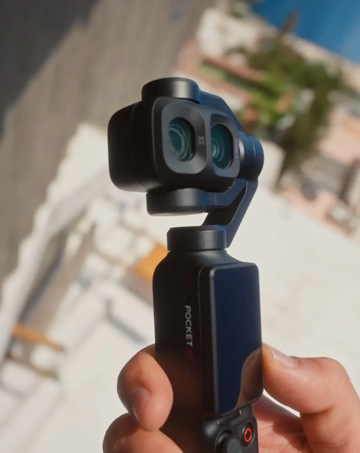 Main tenant l'Osmo Pocket 4P en extérieur au soleil, double objectif tourné vers l'avant