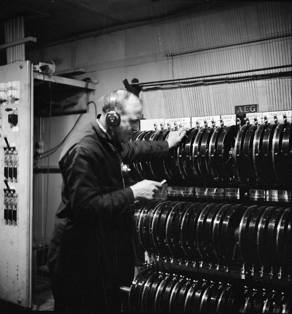 Photo noir et blanc : homme au casque devant une longue rangée de manettes de gradateurs