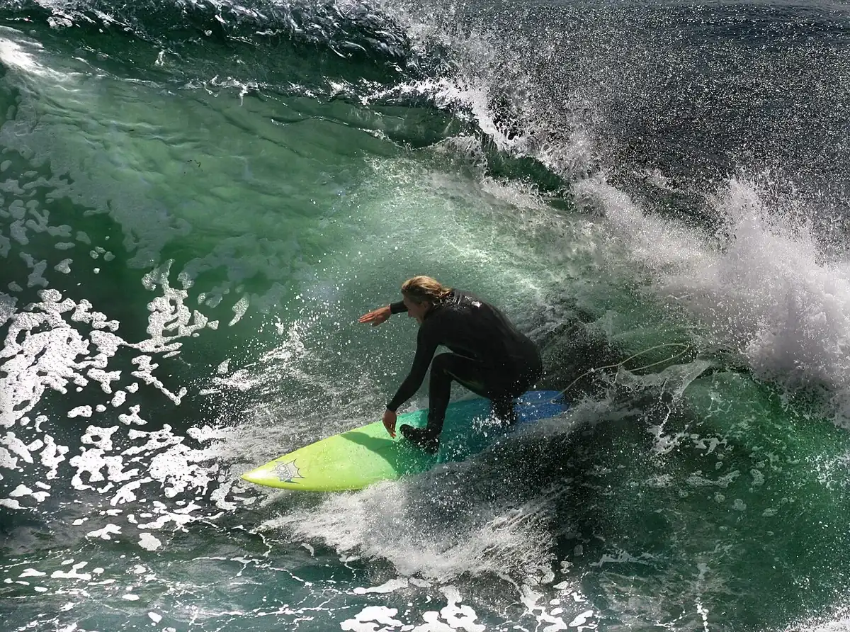 Surfer ajupit al seu tauler verd a l'abeurador d'una onada trencadora