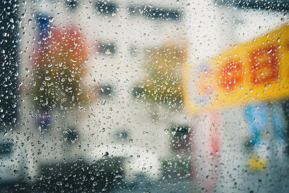 Gouttes de pluie sur une vitre, l’arrière-plan réduit à des taches de lumière floues