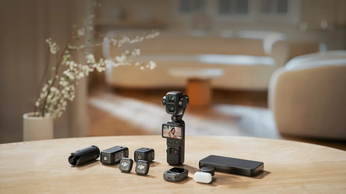 Caméra de poche posée sur une table ronde avec deux micros sans fil, leur boîtier, une lampe d’appoint et une poignée