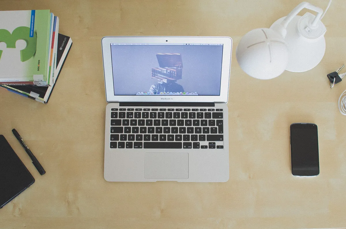 Ordinateur portable ouvert sur un bureau clair, casque, carnets et téléphone