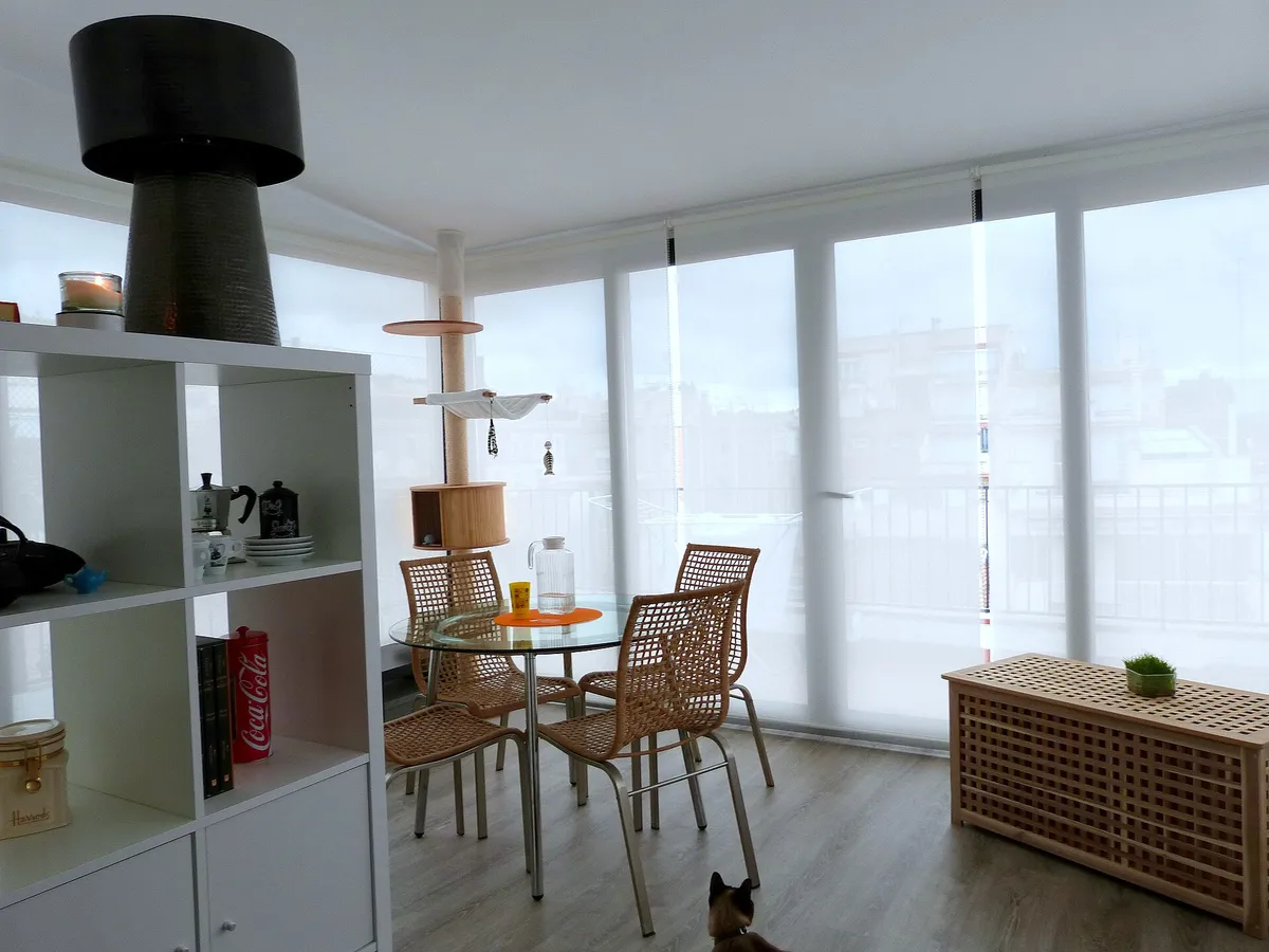 A dining corner in front of large windows, a low shelf unit and a round table