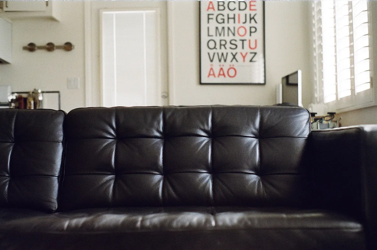 A black leather sofa beneath a framed poster, white wall and pale floor