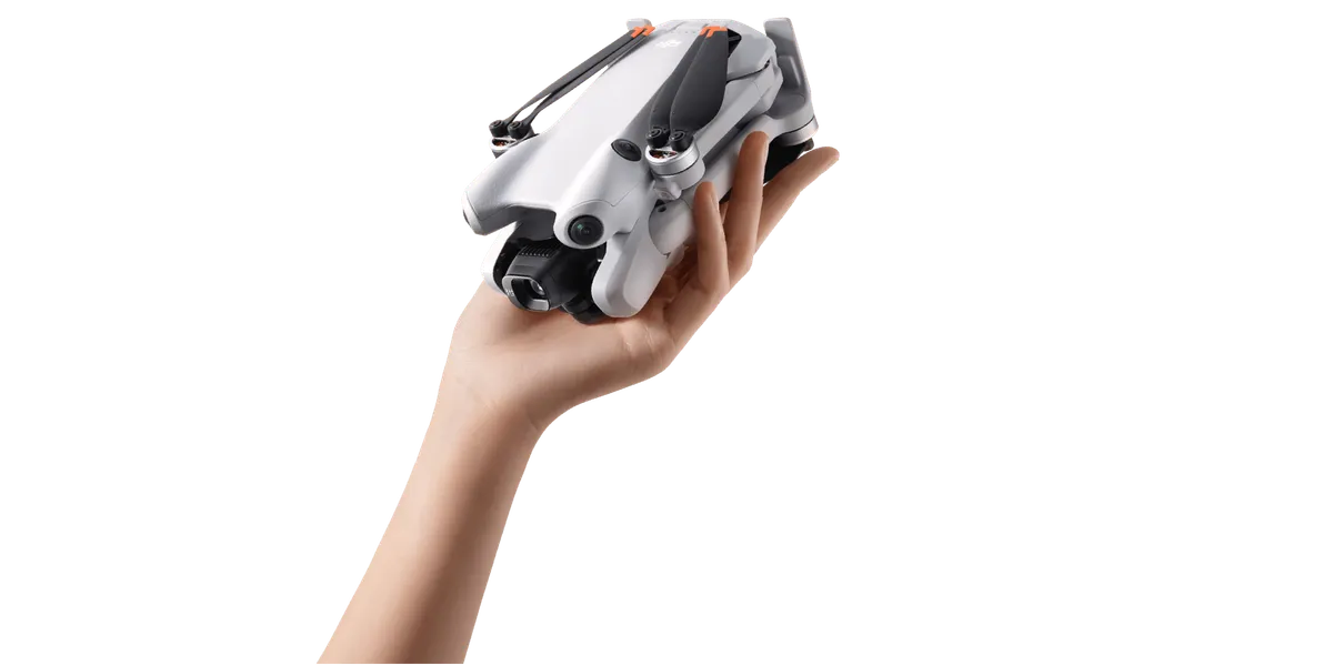Petit drone gris replié tenu dans une main ouverte, sur fond noir