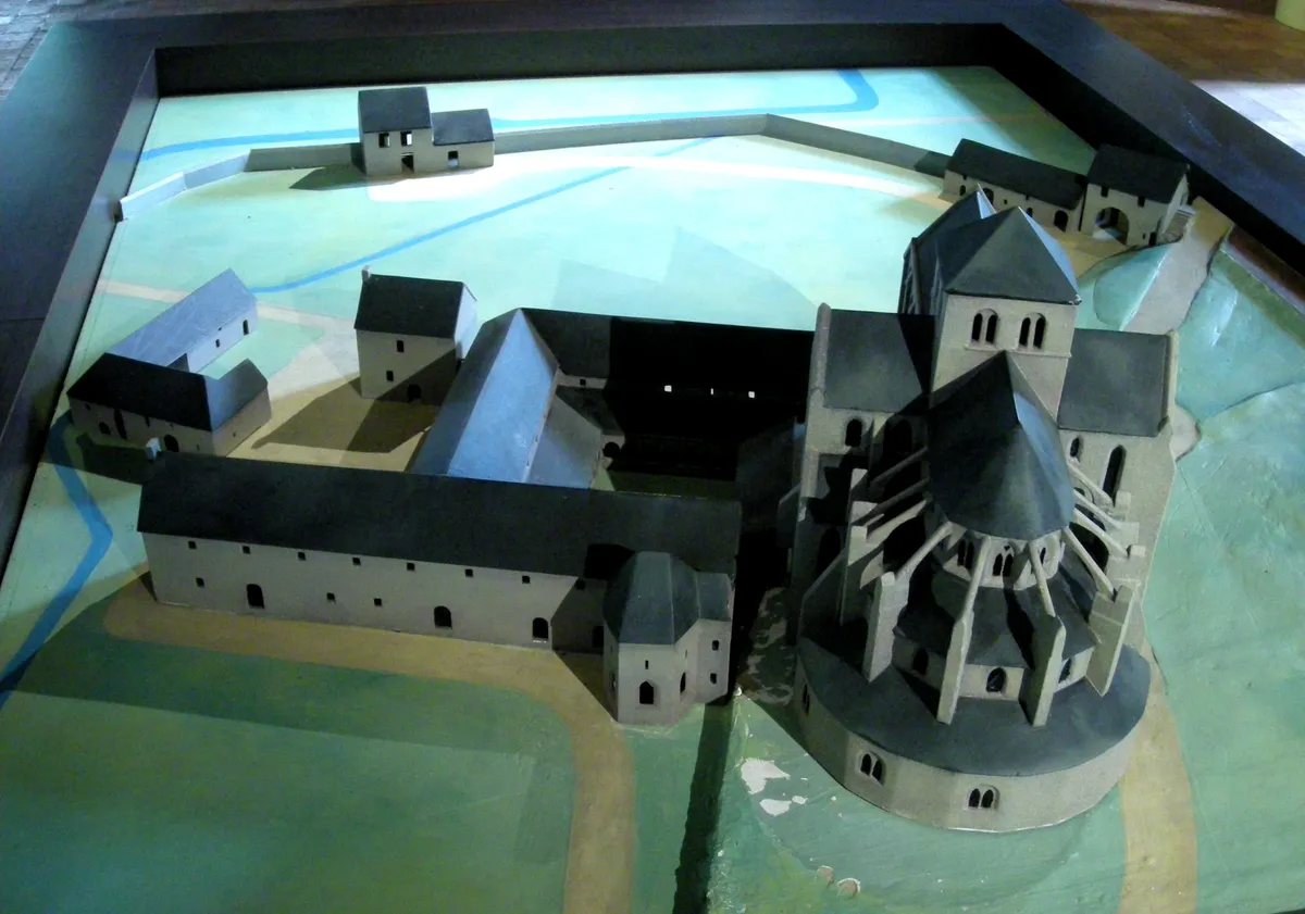 Maquette d’un ensemble monastique en pierre grise sous vitrine, posée sur un plan de terrain peint