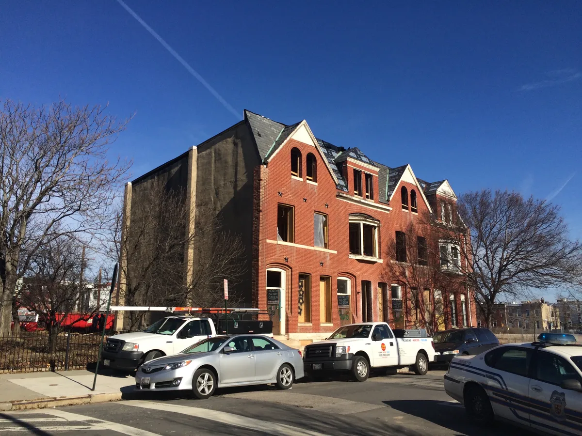 Maisons de ville en brique en cours de réhabilitation : fenêtres sans menuiseries, toiture neuve et véhicules d’artisans devant