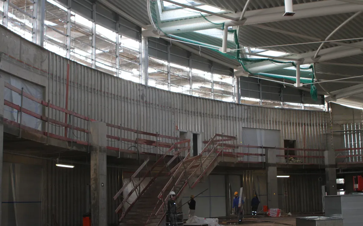 Intérieur d’un bâtiment en construction : escalier métallique, garde-corps provisoires et ouvriers casqués