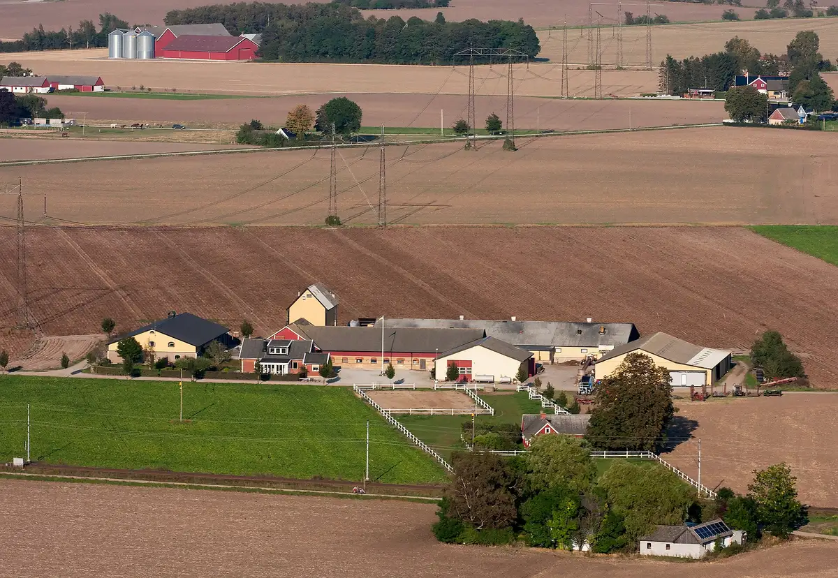 Una masia i els seus edificis vistos des de l’aire, travessada per una línia elèctrica i les seves torres