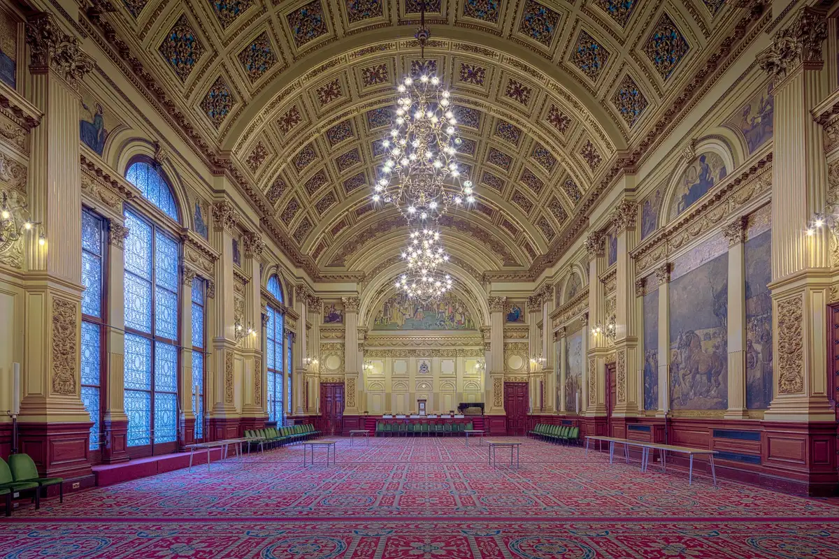 A large empty function room, a central chandelier, red carpet and tall windows